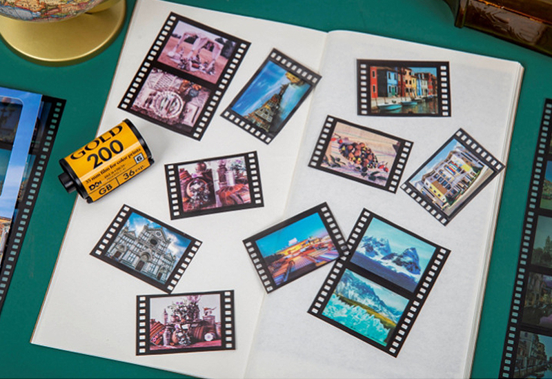 Einzelne Film-Sticker mit Reise- und Stadtmotiven auf einem aufgeschlagenen Notizbuch verteilt